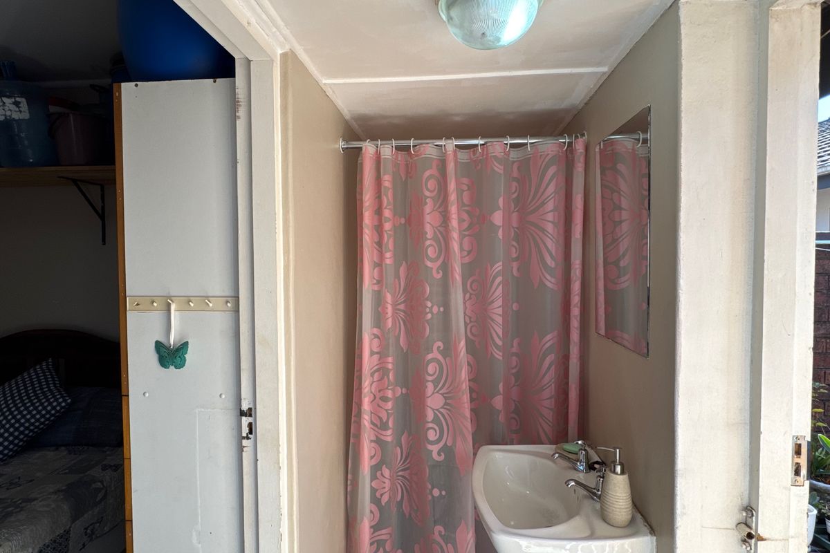 A compact bathroom featuring a wall-mounted basin with chrome tapware and a shower area enclosed by a curtain.