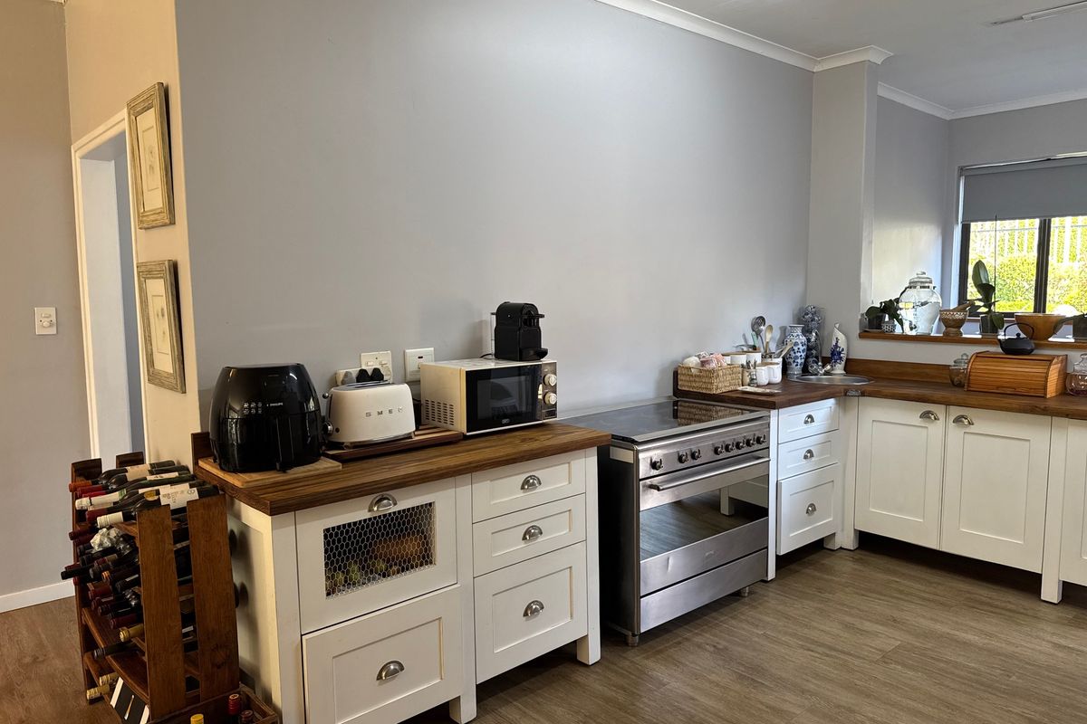 A functional kitchen featuring white cabinetry, warm wooden countertops, a freestanding oven, and durable laminate flooring, offering a clean and practical workspace.