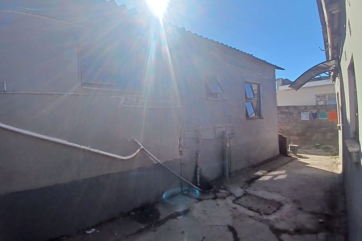 A view of the rear exterior area showing concrete paving, external plumbing, and boundary walls with weathered finishes.