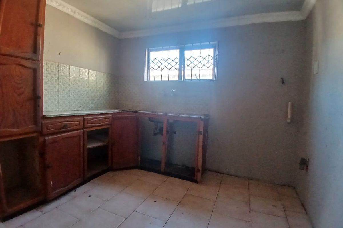 A dated, empty kitchen space featuring wooden cabinetry, tiled splashbacks, and tiled flooring, requiring significant renovation and modernization to restore functionality.