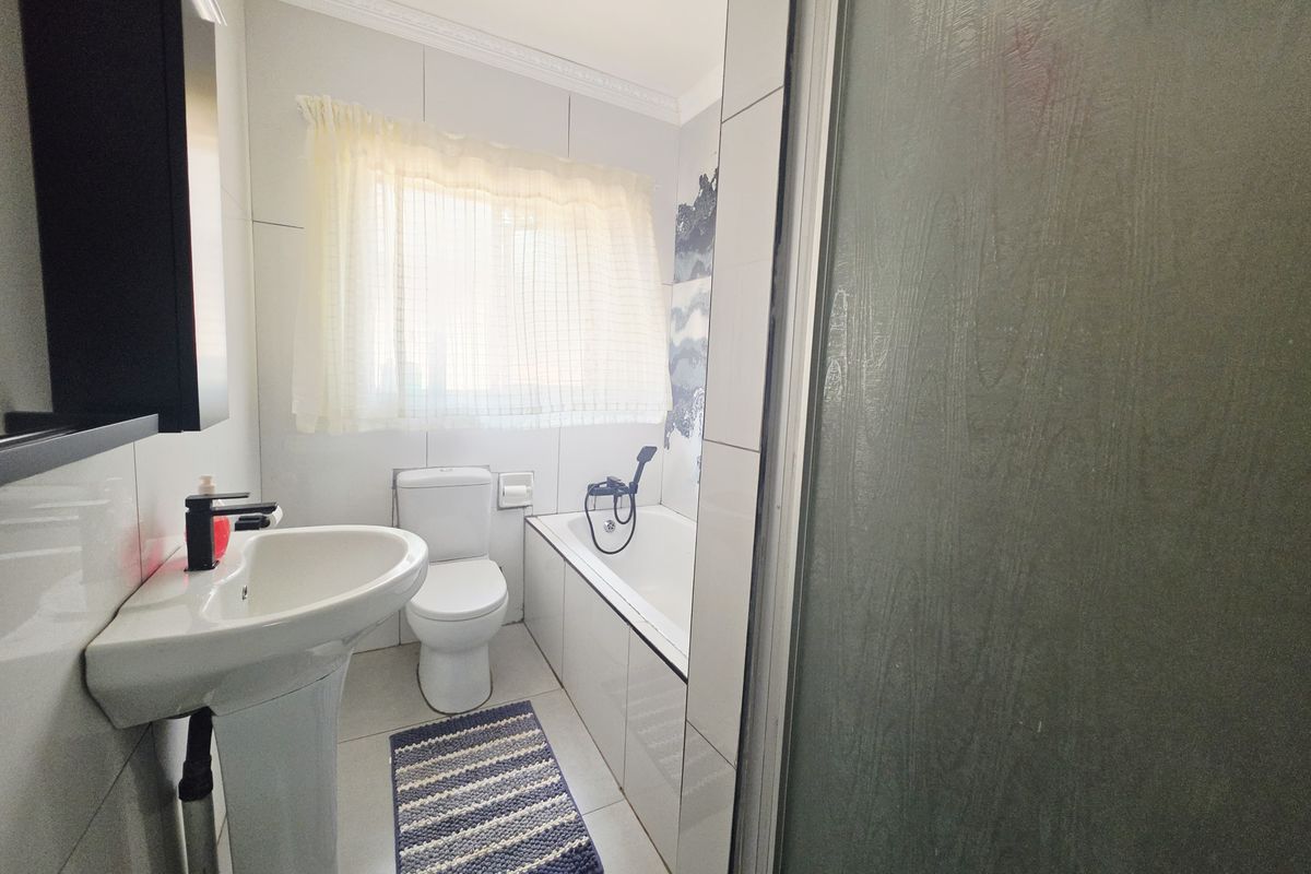 A functional bathroom featuring a pedestal basin, toilet, and a bathtub with a shower screen, finished with neutral wall and floor tiles.