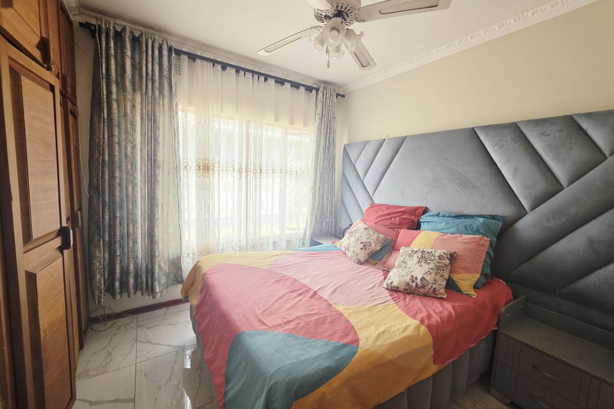 A well-maintained bedroom featuring built-in wooden cupboards, tiled flooring, and a ceiling fan, offering a comfortable and functional living space.