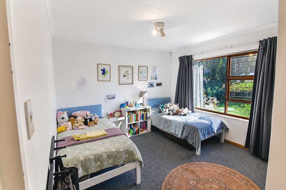 A functional bedroom featuring carpeted flooring, a large window with security bars, and a ceiling light fixture.