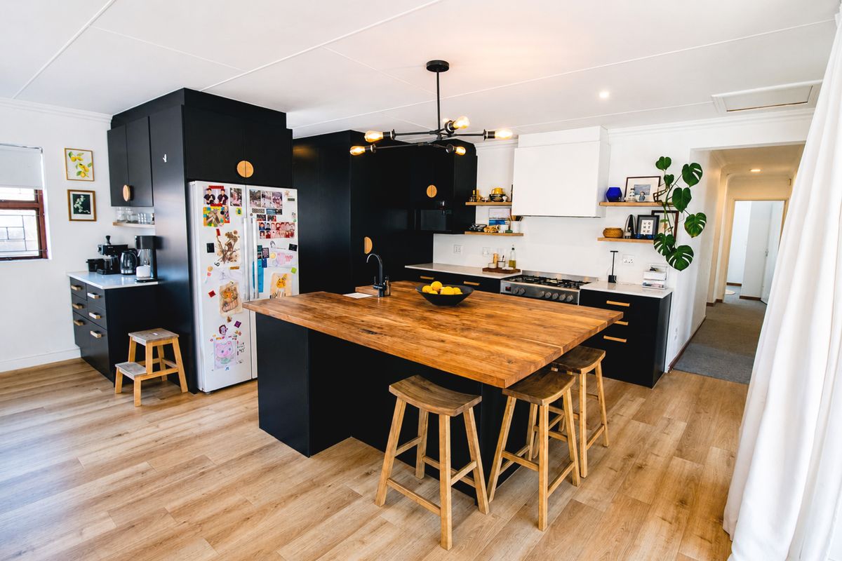 Modern kitchen featuring a large wooden island, sleek black cabinetry, gas hob, and integrated extractor fan, complemented by warm laminate flooring.