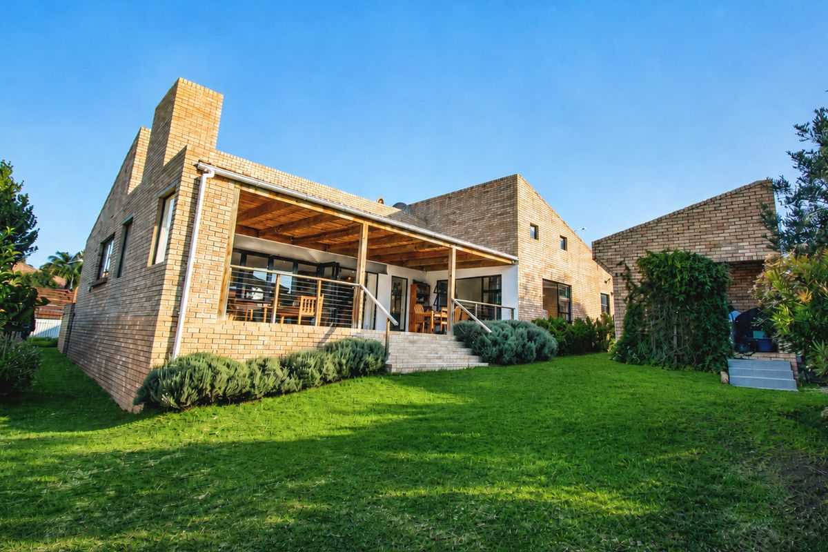 Rear view of a brick house featuring a covered patio with timber pergola, stone steps, and a well-maintained lawn.