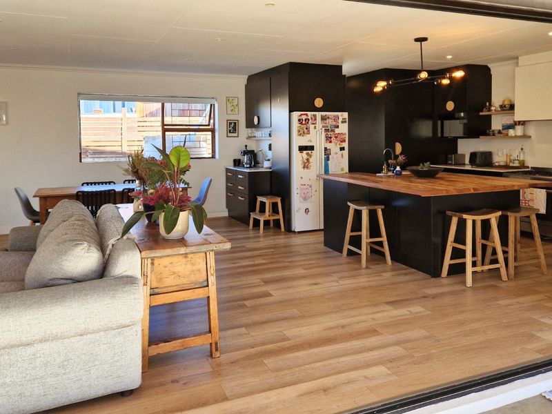 Spacious open-plan living and kitchen area featuring a modern kitchen island with timber countertop, sleek black cabinetry, and light wood-look flooring.