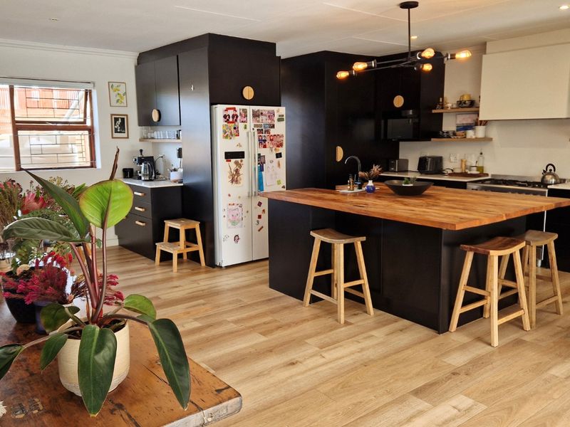 Modern open-plan kitchen featuring a large island with a butcher block countertop, dark cabinetry, and high-quality laminate flooring.