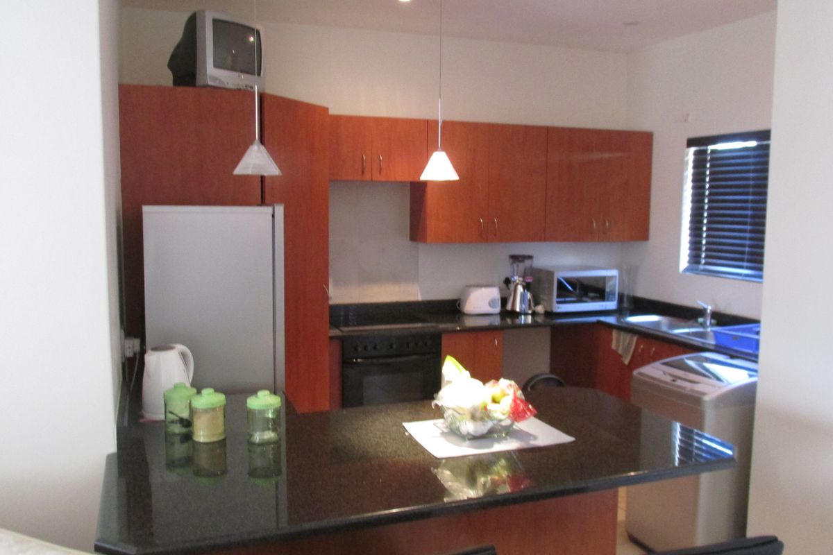 A functional kitchen featuring wood-finish cabinetry, dark granite countertops, integrated oven and hob, and a breakfast bar area.