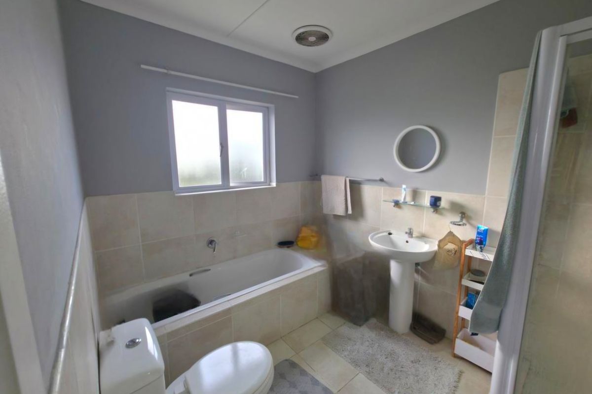 A functional bathroom featuring a pedestal basin, built-in bathtub, toilet, and a separate shower enclosure with neutral wall and floor tiling.