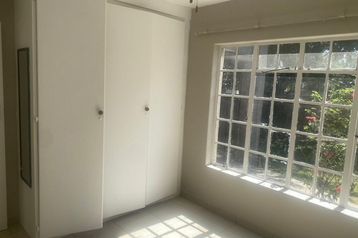 A bright, empty bedroom featuring built-in cupboards and a large grid-pane window overlooking the garden.