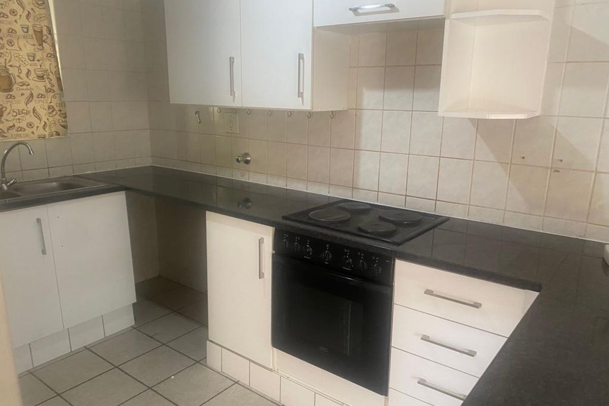A functional kitchen featuring white cabinetry, dark countertops, an integrated electric hob and oven, and tiled splashbacks.