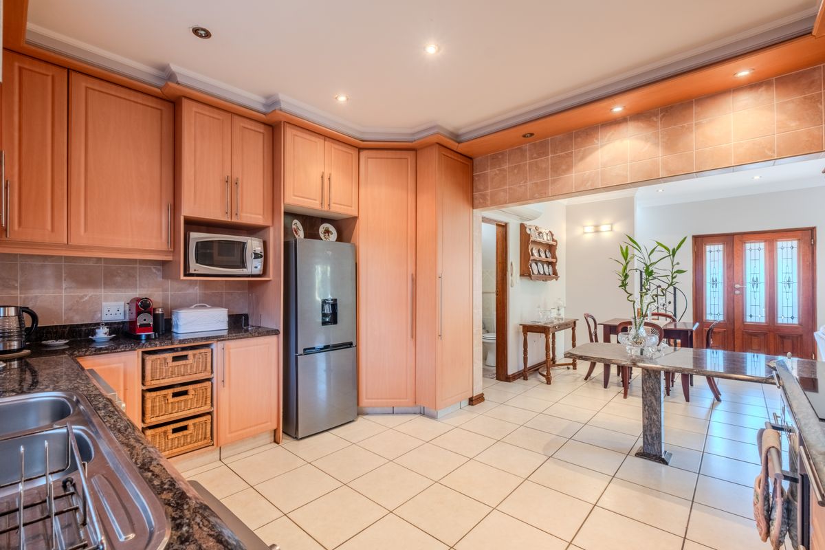 A functional kitchen featuring light wood cabinetry, granite countertops, tiled flooring, and a built-in microwave, with an open-plan flow into the dining area.