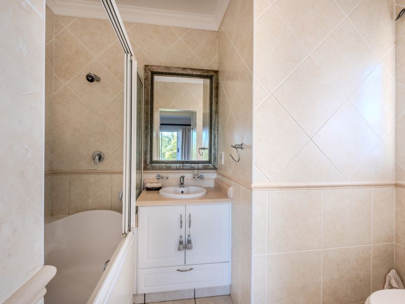 A well-maintained bathroom featuring a built-in vanity, shower-over-bath combination, and neutral ceramic wall tiling throughout.