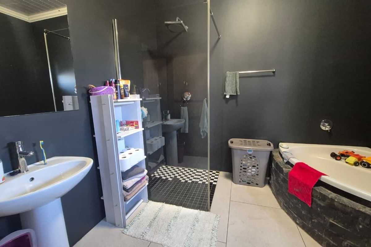 A bathroom featuring a pedestal basin, a glass-enclosed shower with mosaic floor tiles, and a built-in corner bathtub with dark stone-look cladding.