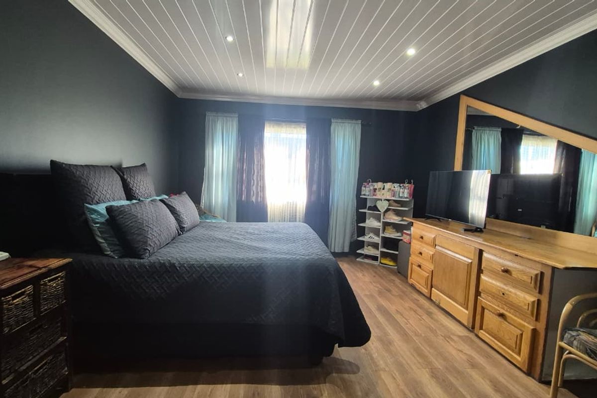 Spacious bedroom featuring dark painted walls, wood-look laminate flooring, and a white tongue and groove ceiling with recessed lighting.