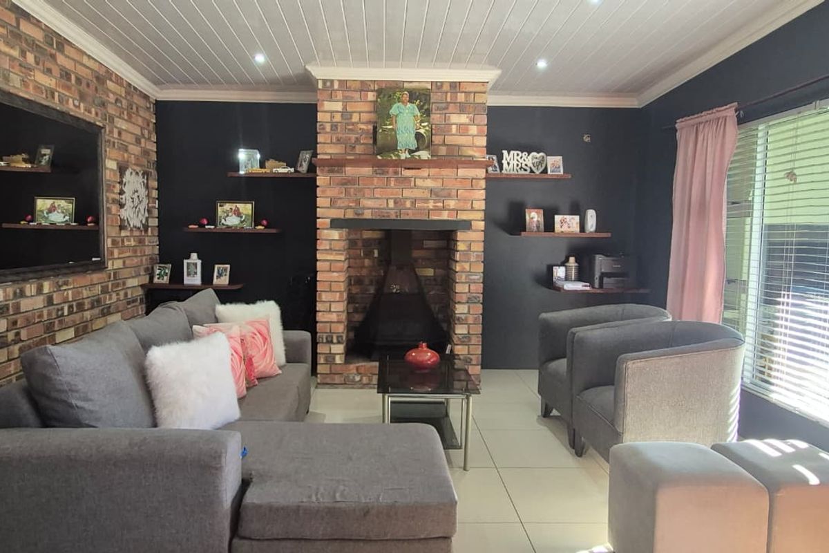 A cozy living room featuring a prominent brick fireplace, exposed brick accent wall, tiled flooring, and timber ceiling paneling with recessed lighting.