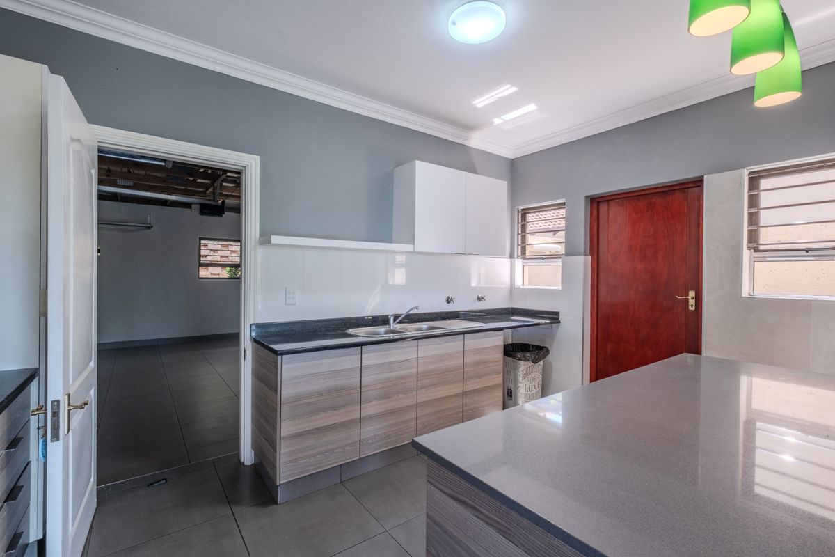 Modern kitchen featuring wood-grain cabinetry, stone countertops, a central island, and tiled flooring, with direct access to an adjacent utility or garage space.