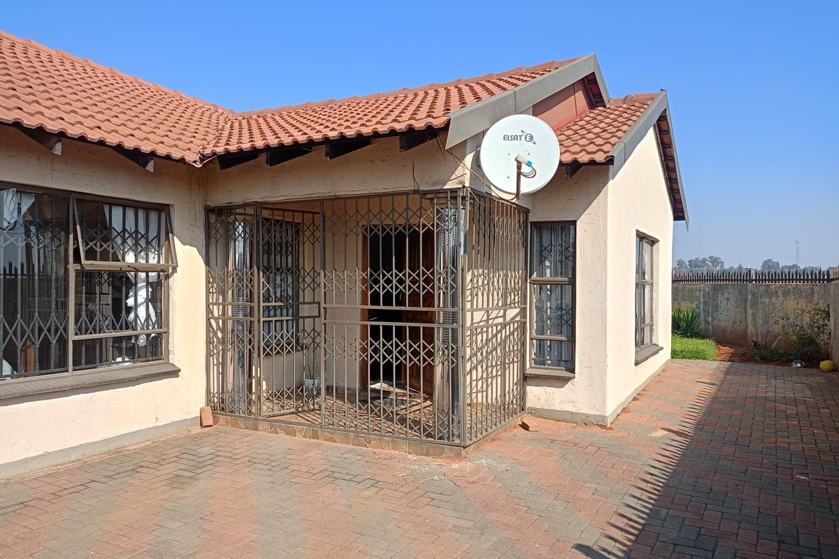 Rear exterior view of the house featuring a paved patio area, security gates, and a tiled roof.