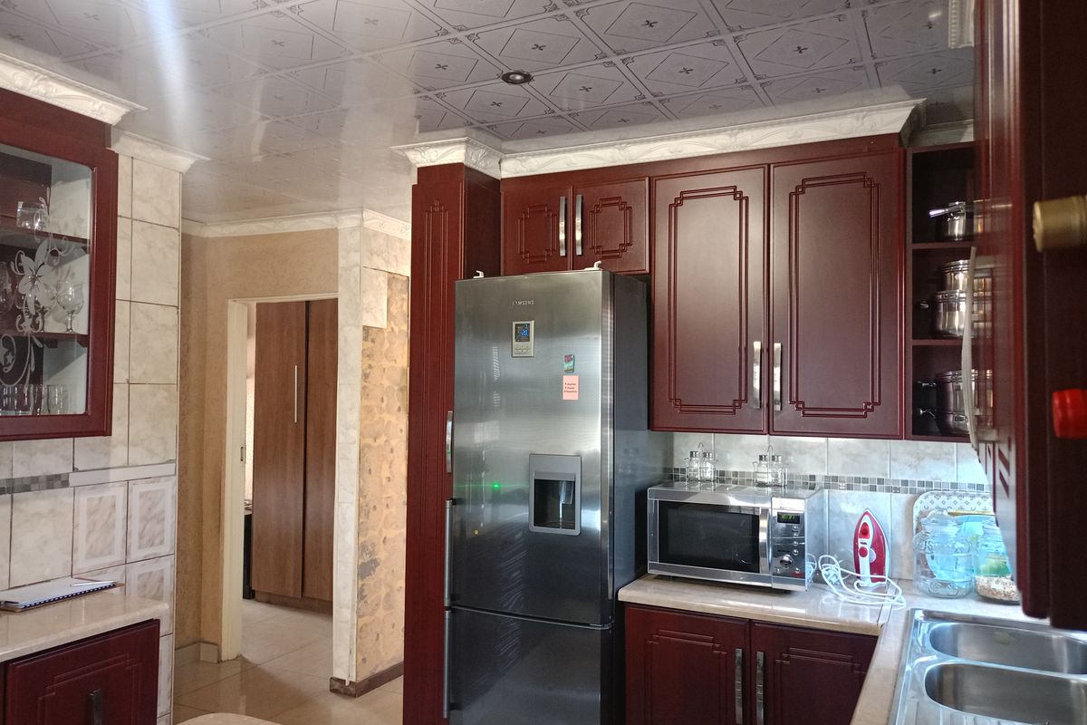 A functional kitchen featuring dark wood cabinetry, laminate countertops, a double stainless steel sink, and decorative ceiling tiles, with some visible wall wear.