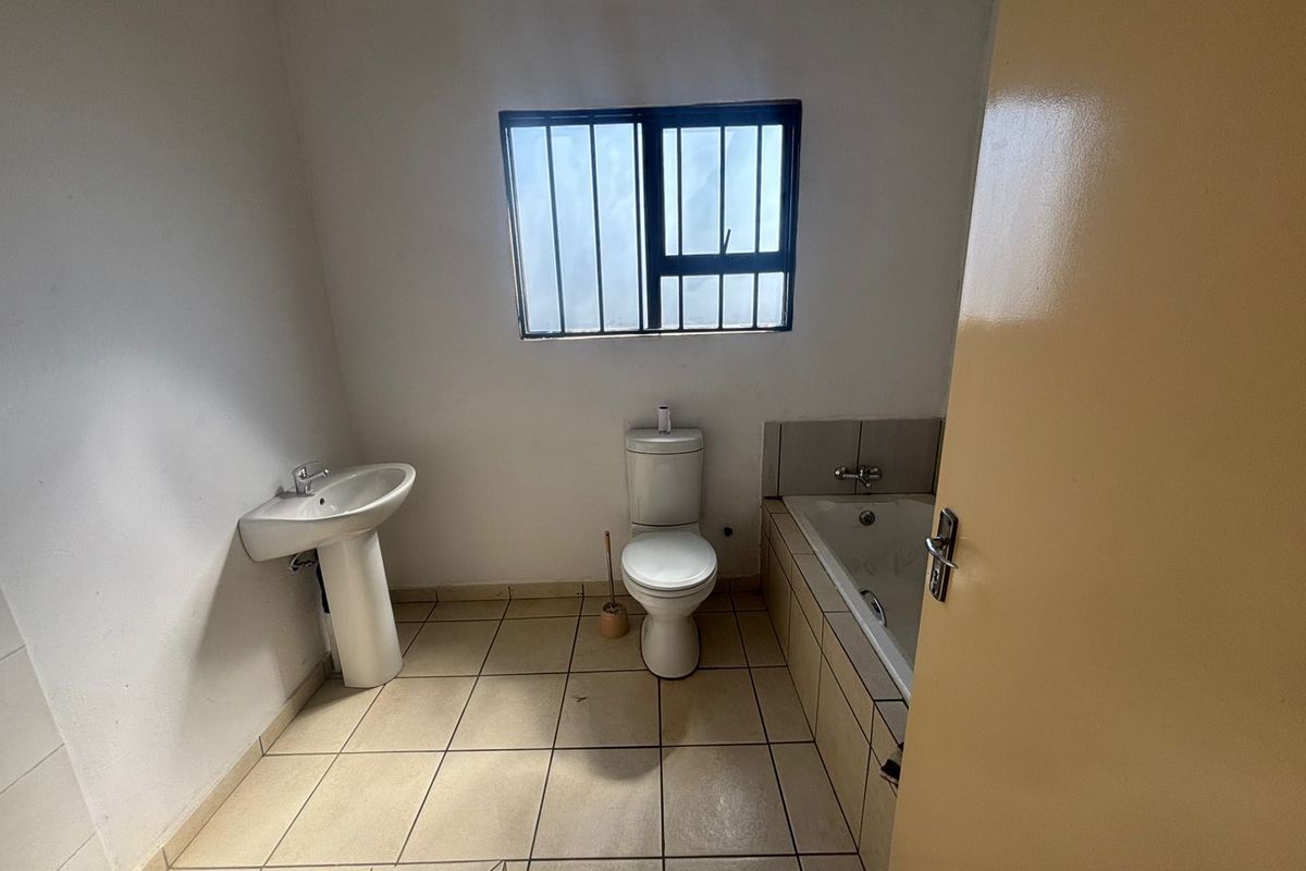 A functional bathroom featuring a pedestal basin, toilet, and built-in bathtub with tiled flooring and security bars on the window.