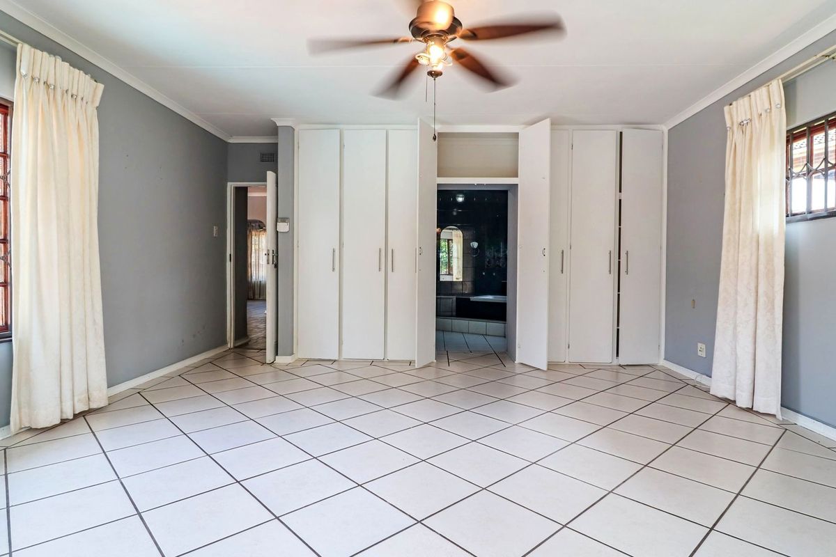 Spacious bedroom featuring tiled flooring, built-in cupboards, and a ceiling fan, with direct access to an en-suite bathroom.