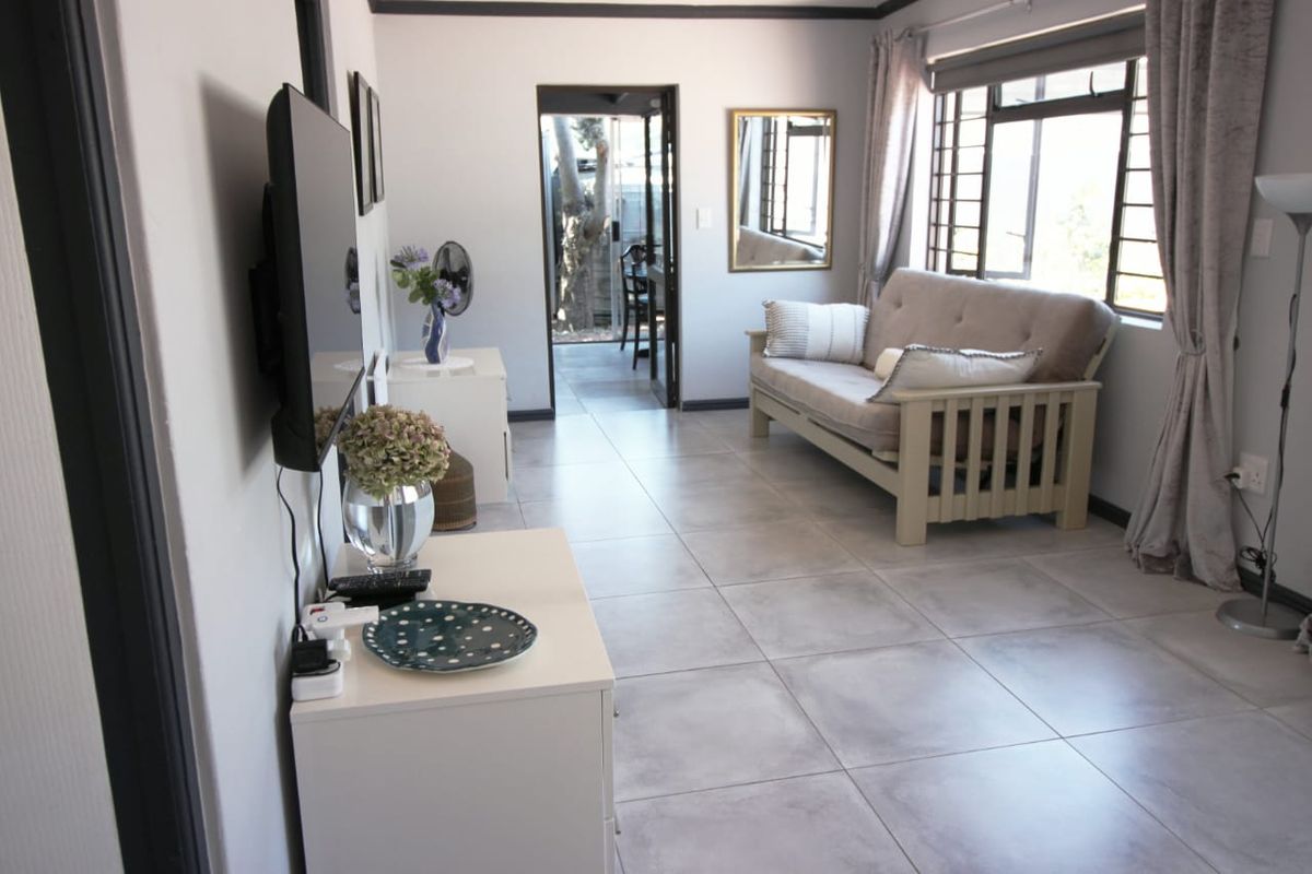 A bright living room featuring large format floor tiles, security bars on windows, and direct access to an outdoor patio area.