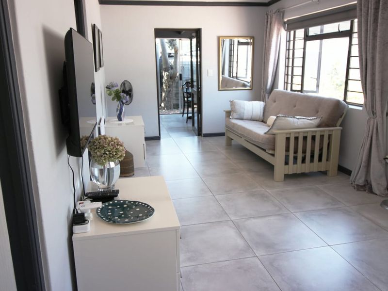 A bright living room featuring large format floor tiles, security bars on windows, and direct access to an outdoor patio area.
