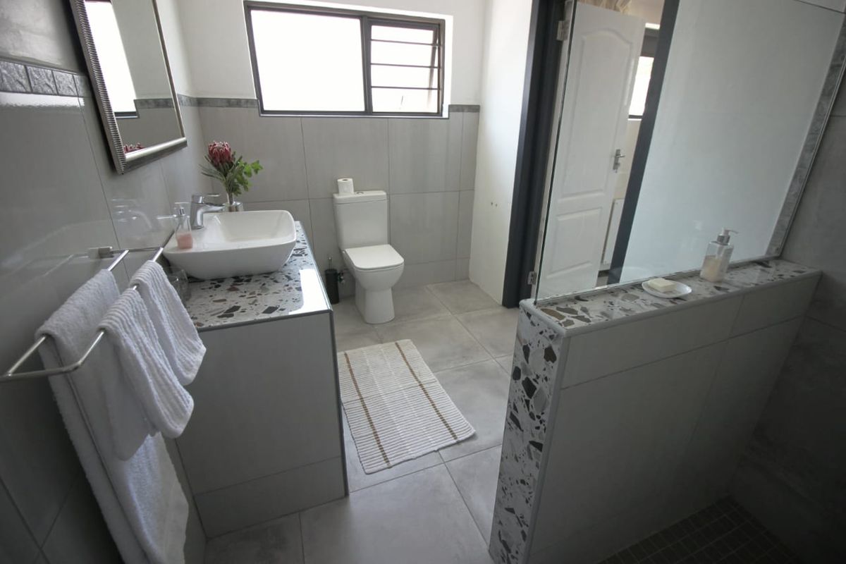 Modern bathroom featuring a terrazzo-topped vanity with a vessel sink, tiled finishes, and a glass-partitioned shower area.