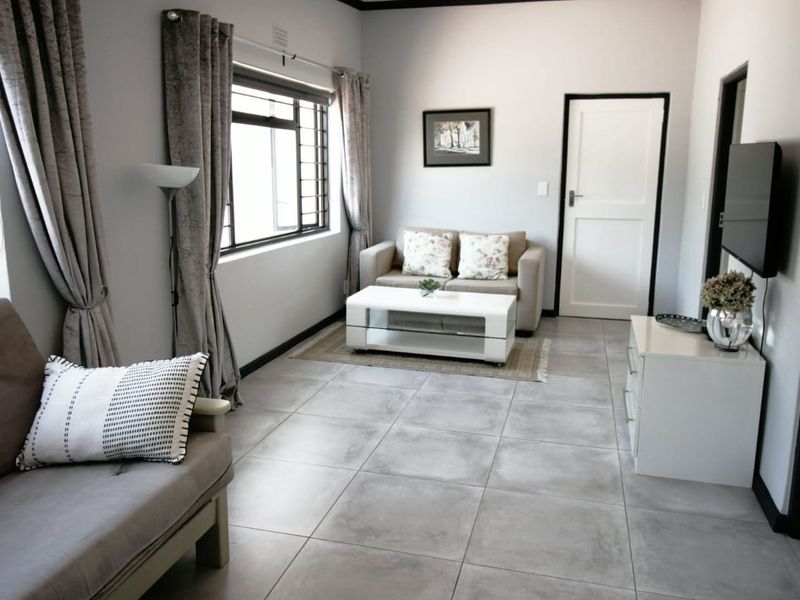 A well-maintained living room featuring neutral tiled flooring, large windows with security bars, and a clean, modern aesthetic.