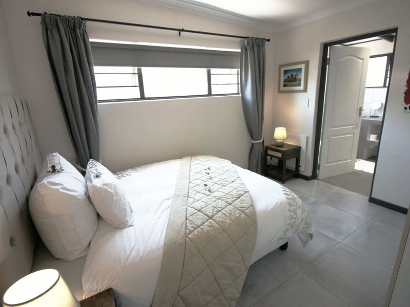 A well-maintained bedroom featuring tiled flooring, a horizontal window with security bars, and direct access to an adjoining bathroom.