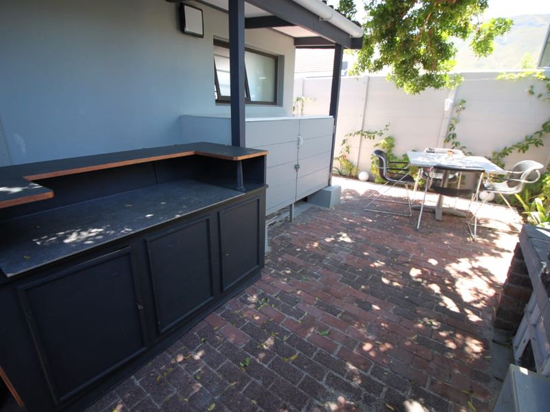 A covered outdoor patio area featuring built-in cabinetry, brick paving, and a boundary wall, providing a functional space for outdoor entertaining.