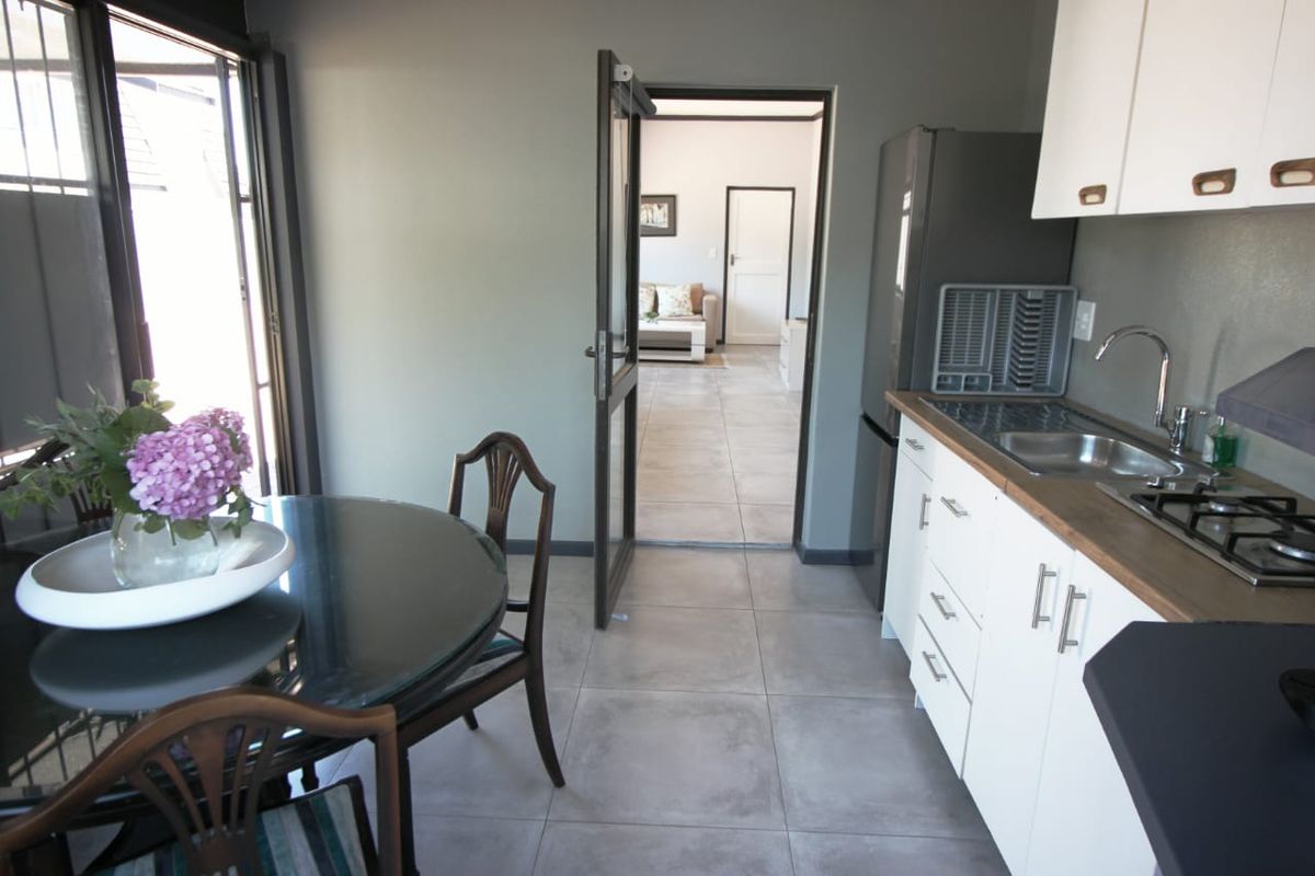 A functional kitchen featuring white cabinetry, a gas hob, and tiled flooring, with direct access to an adjacent living area through a doorway.