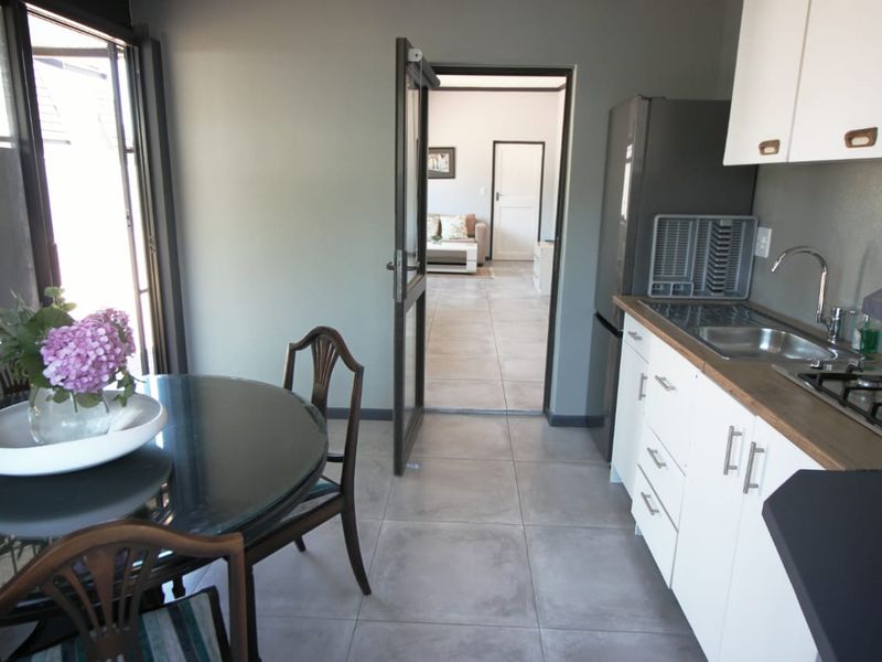 A functional kitchen featuring white cabinetry, a gas hob, and tiled flooring, with direct access to an adjacent living area through a doorway.
