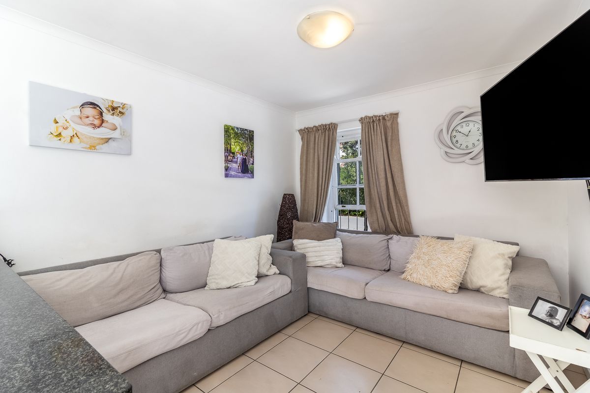 A living area featuring tiled flooring, a wall-mounted television, and a window with curtains.