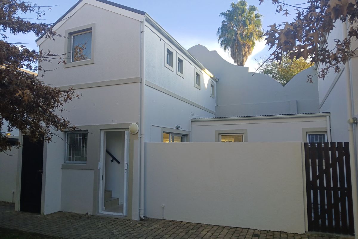 A view of the rear exterior of the apartment building, featuring a paved courtyard area, white rendered walls, and a secure wooden gate.