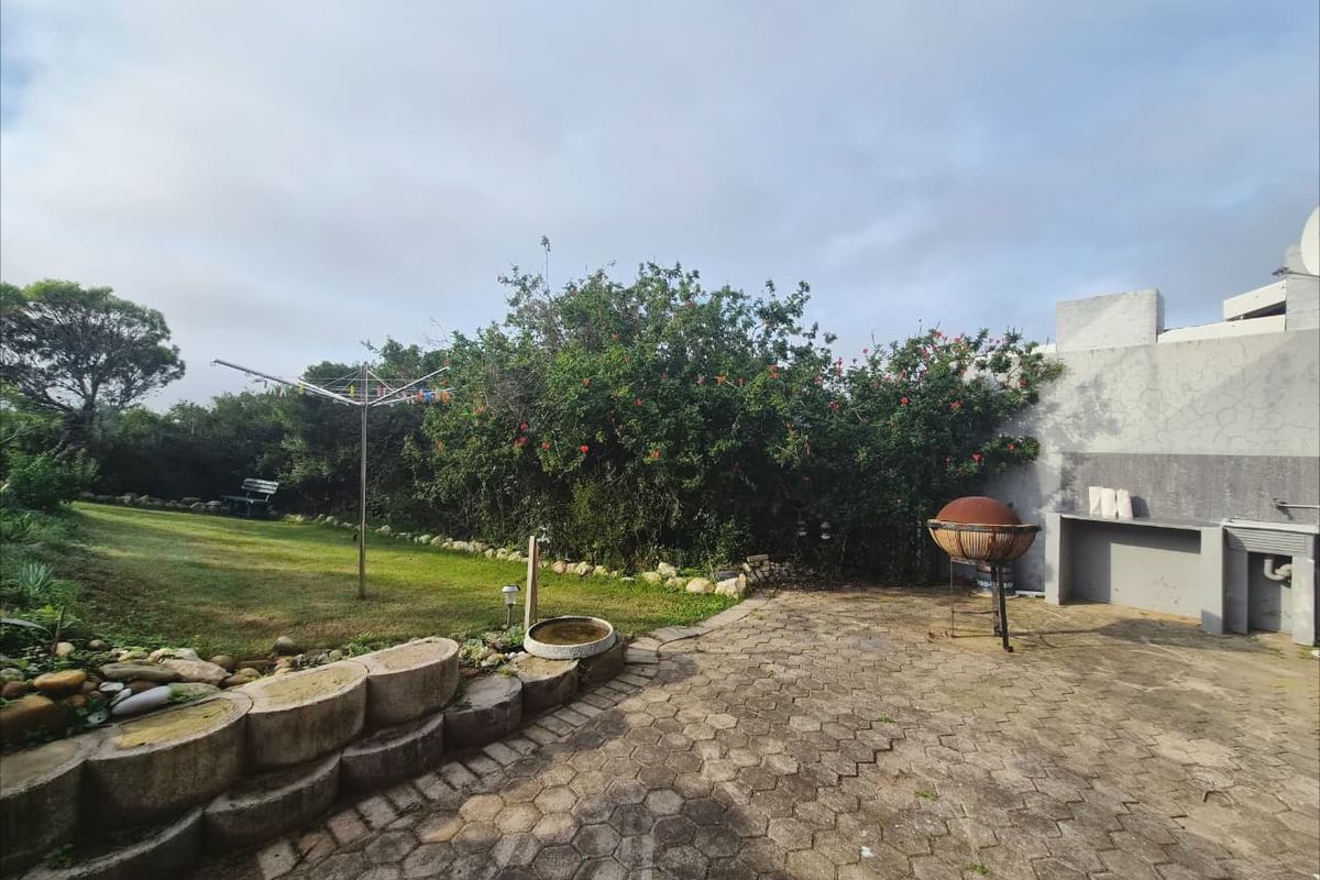 Rear garden area featuring a paved patio, built-in braai, and established lawn with a retaining wall.