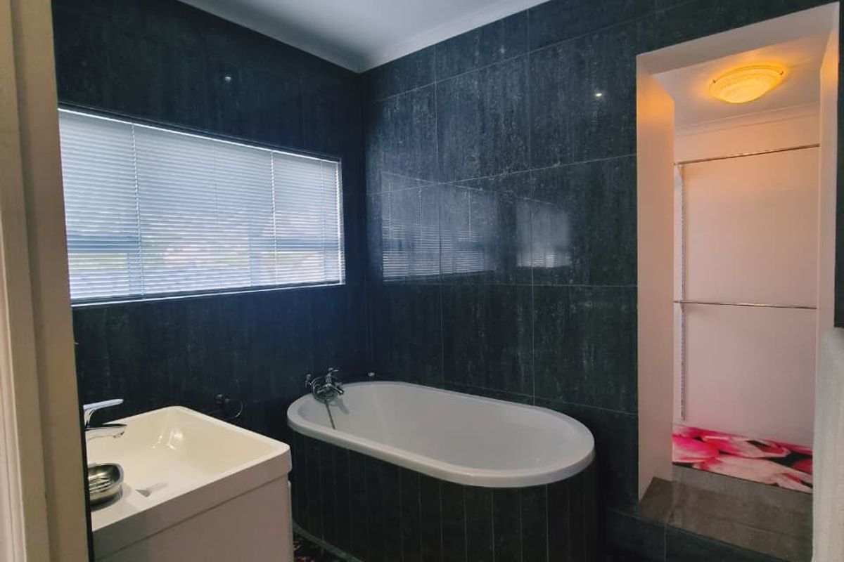 Modern bathroom featuring dark tiled walls, a freestanding bathtub, vanity basin, and recessed lighting, with an adjacent walk-in shower area.