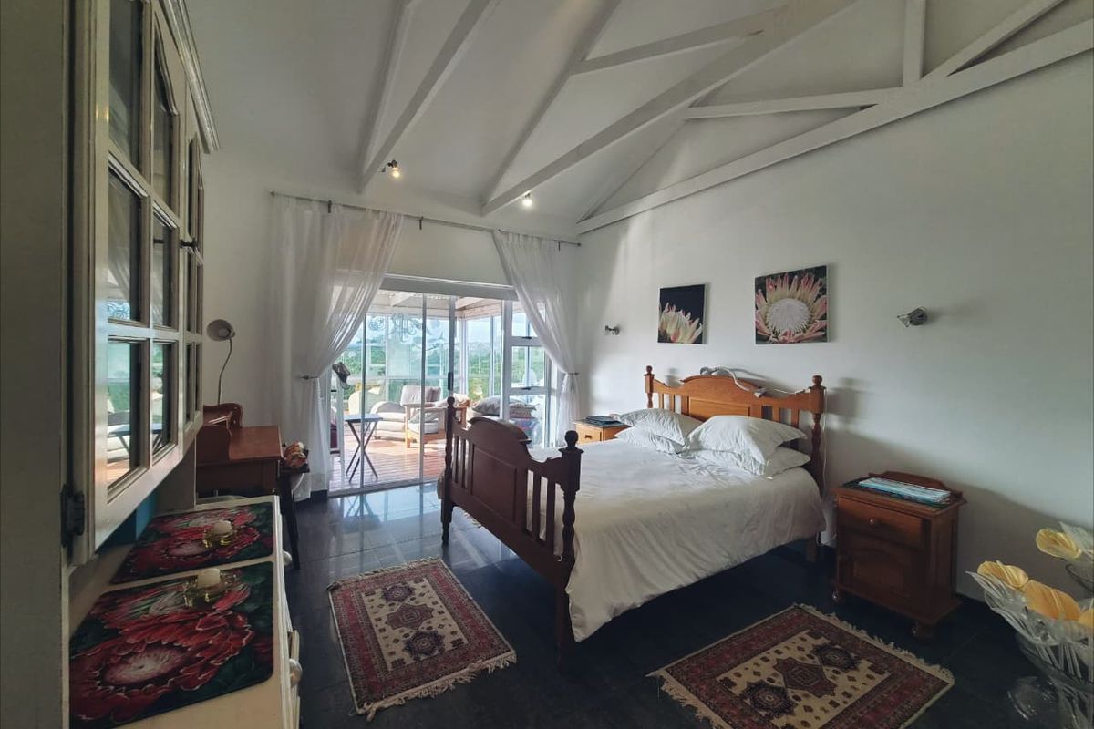 Spacious bedroom featuring a vaulted ceiling with exposed rafters, tiled flooring, and sliding glass doors providing access to an outdoor patio area.