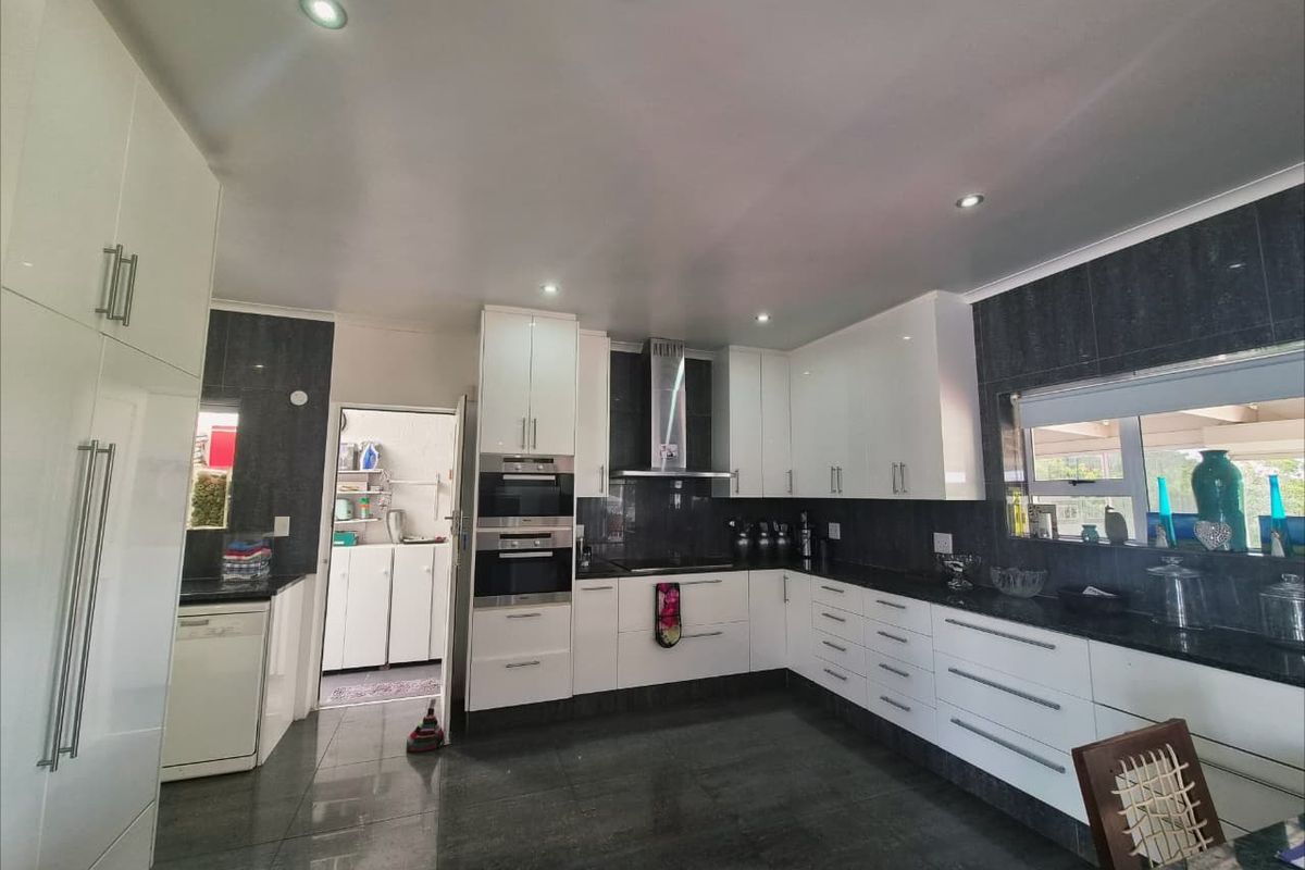 Modern kitchen featuring high-gloss white cabinetry, dark granite countertops, built-in appliances, and sleek tiled flooring with recessed lighting.