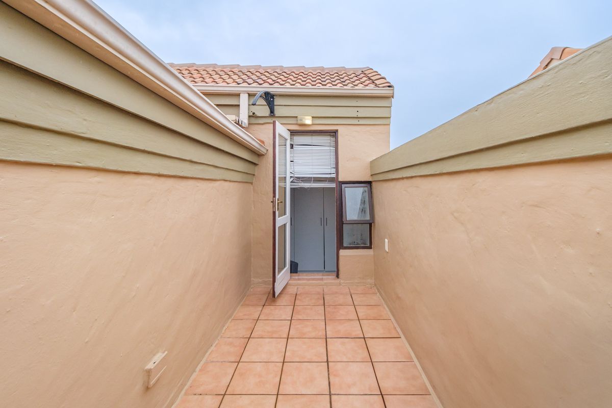 A narrow rear exterior courtyard featuring tiled flooring, accessible via a single door, with surrounding boundary walls and tiled roof eaves.