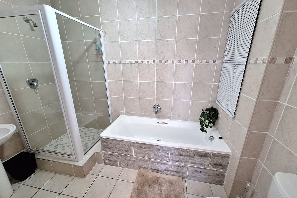 A functional bathroom featuring a separate shower enclosure, a built-in bathtub with tiled surround, and neutral wall and floor tiling.