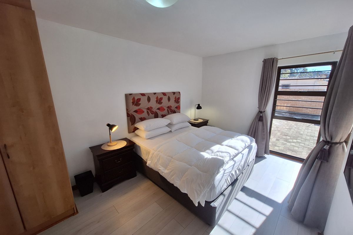 A well-lit bedroom featuring laminate flooring, a built-in wardrobe, and a large window providing natural light and access to the exterior.