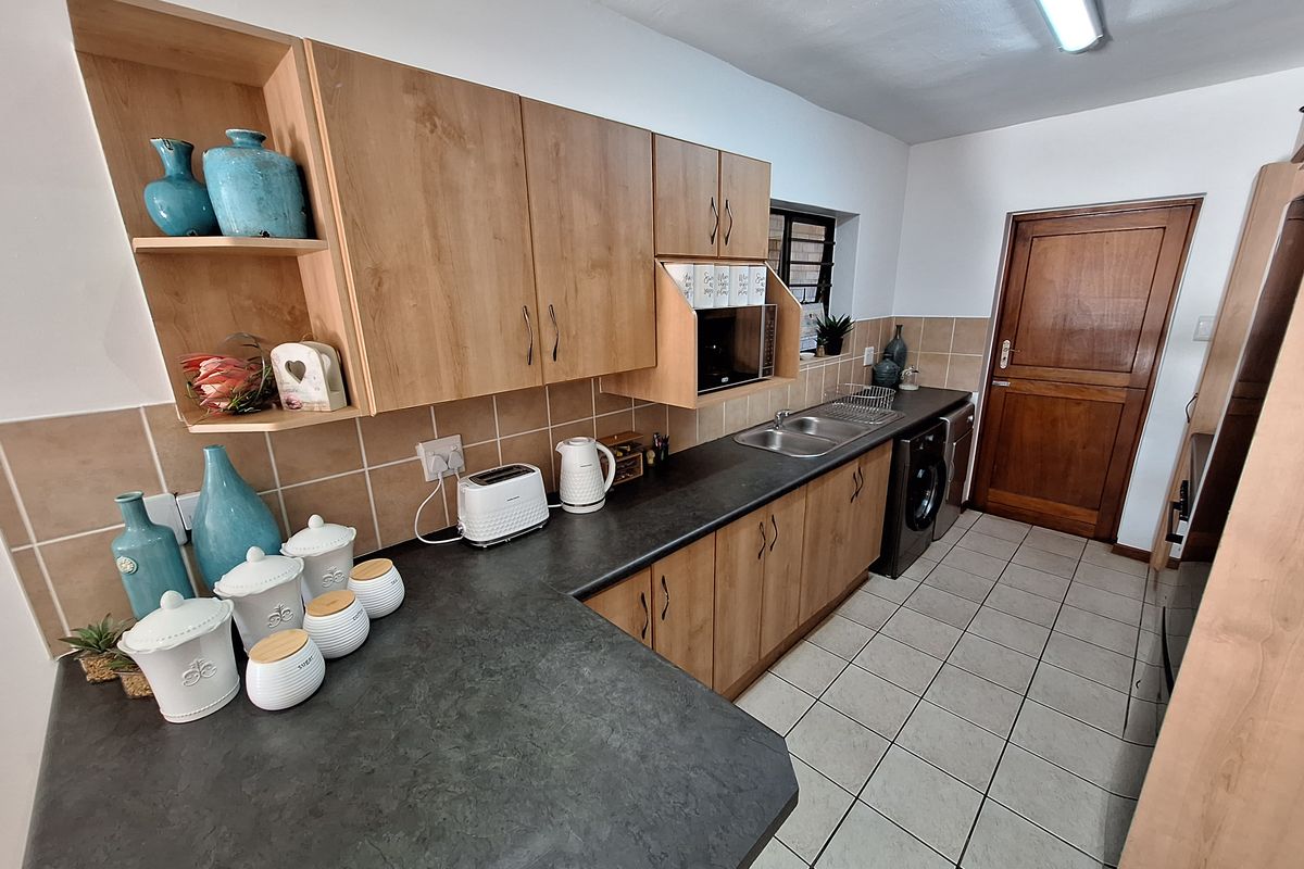 Functional kitchen featuring wood-look laminate cabinetry, dark countertops, tiled backsplash, and ceramic flooring with integrated sink and microwave space.