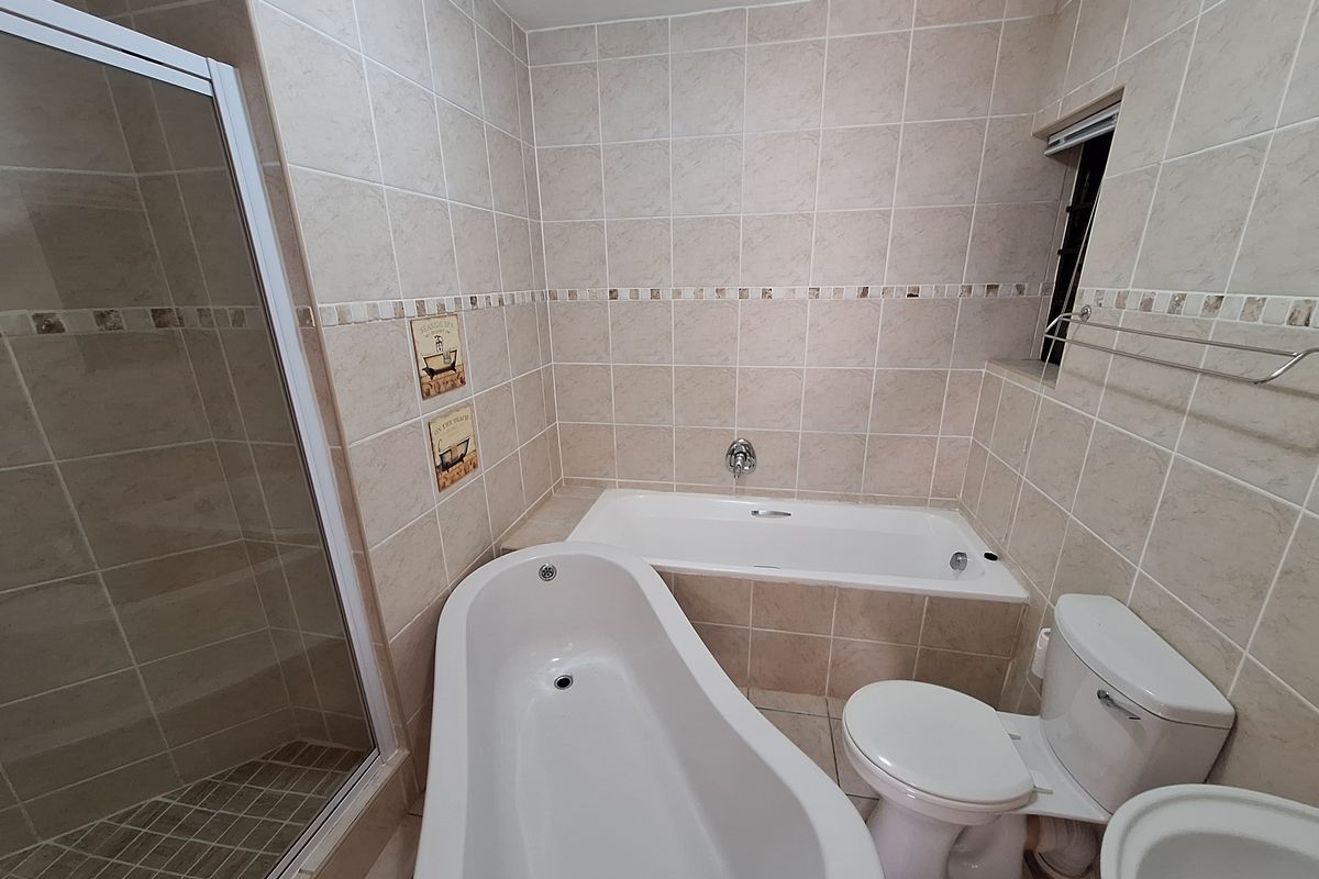 A functional bathroom featuring a separate shower enclosure, a built-in bathtub, a freestanding bathtub, and a toilet with neutral wall and floor tiling.