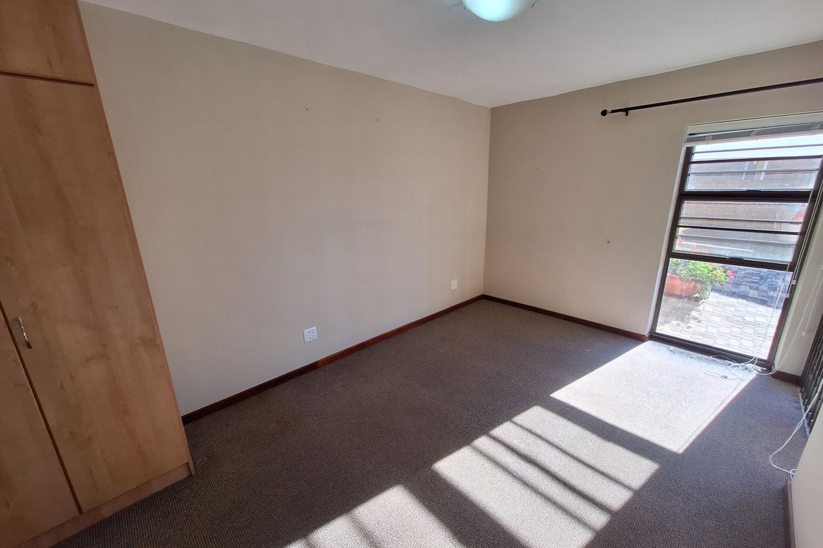 An empty bedroom featuring neutral walls, carpeted flooring, a built-in wardrobe, and a window with security bars allowing natural light.