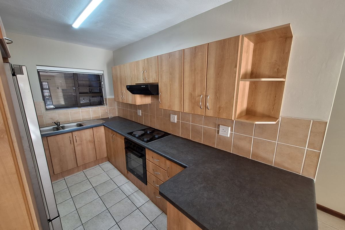 A functional kitchen featuring light wood-finish cabinetry, dark countertops, built-in oven with hob, and tiled flooring, offering a clean and practical workspace.