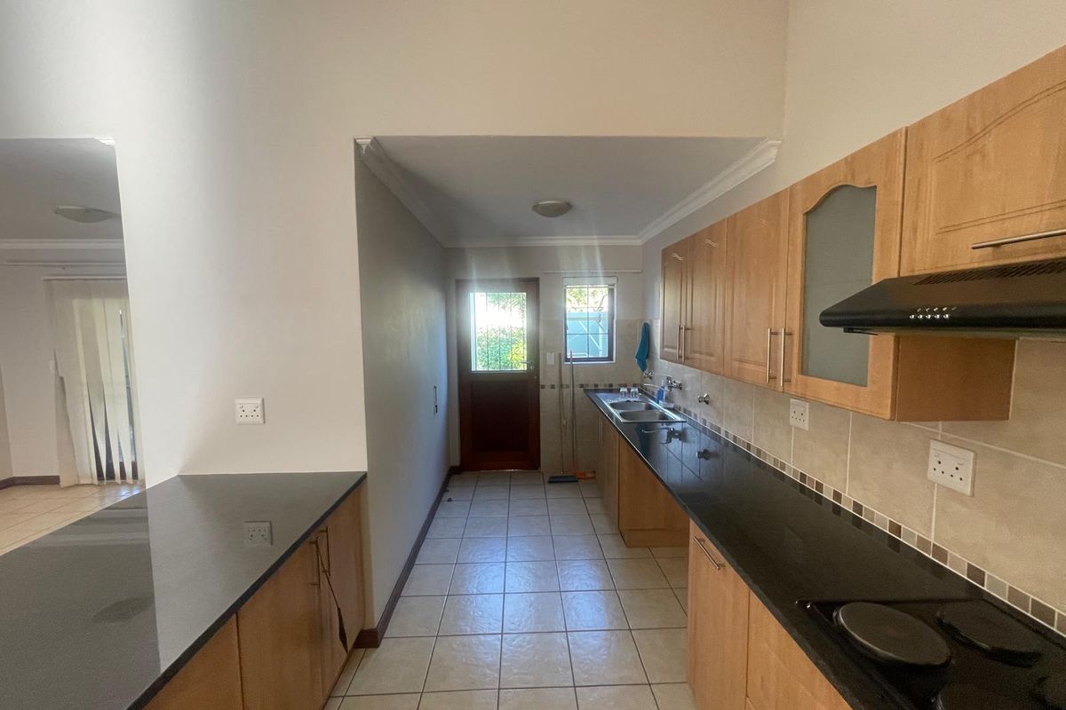 A functional kitchen featuring laminate cabinetry, granite countertops, an electric hob with extractor fan, and direct access to the exterior.