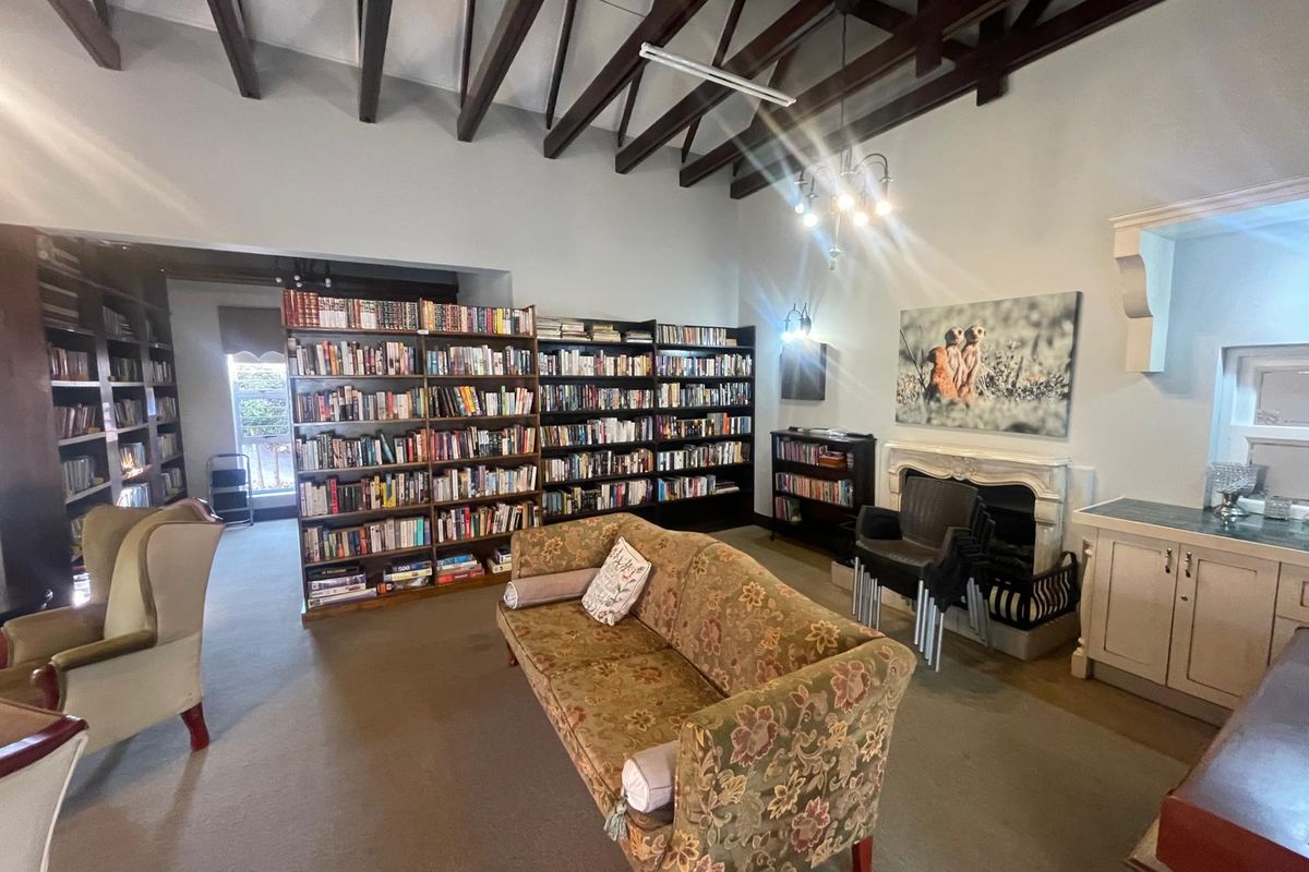 A spacious communal lounge area featuring exposed timber ceiling beams, extensive built-in library shelving, and a decorative fireplace mantel.