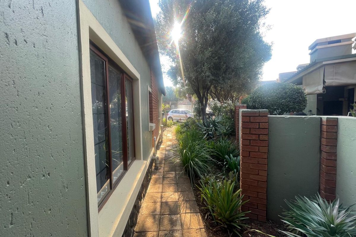 A paved side walkway leading through a landscaped garden area, featuring brick boundary walls and established greenery alongside the property exterior.