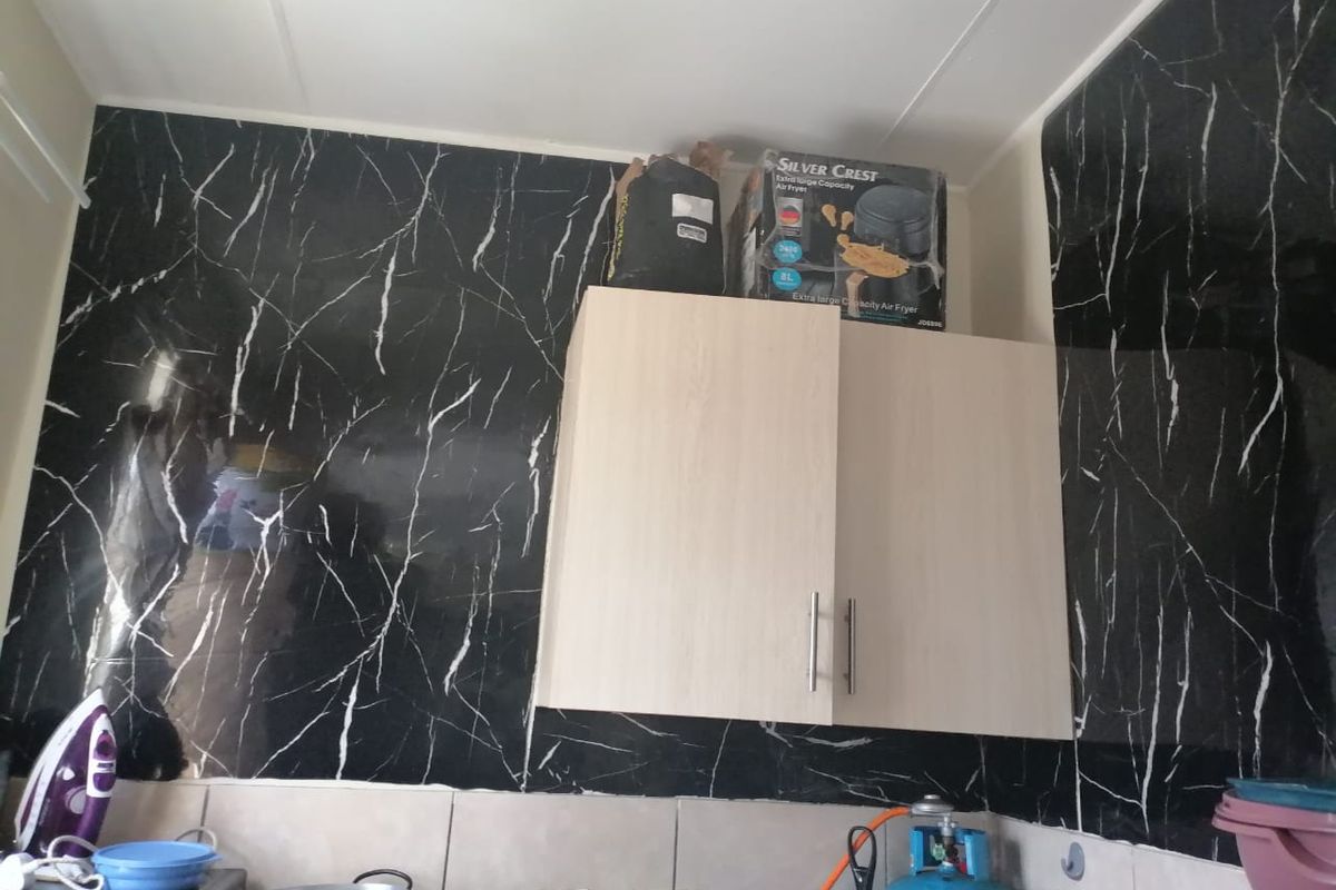 Kitchen area featuring light wood-finish wall-mounted cabinetry set against striking black marble-effect tiled splashbacks.